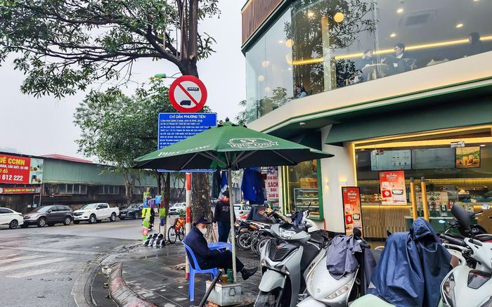 Tại đường Trần Quốc Hoàn (quận Cầu Giấy), một hộ kinh doanh đặt ô che khuất biển chỉ dẫn, gây cản trở tầm nhìn của người tham gia giao thông.